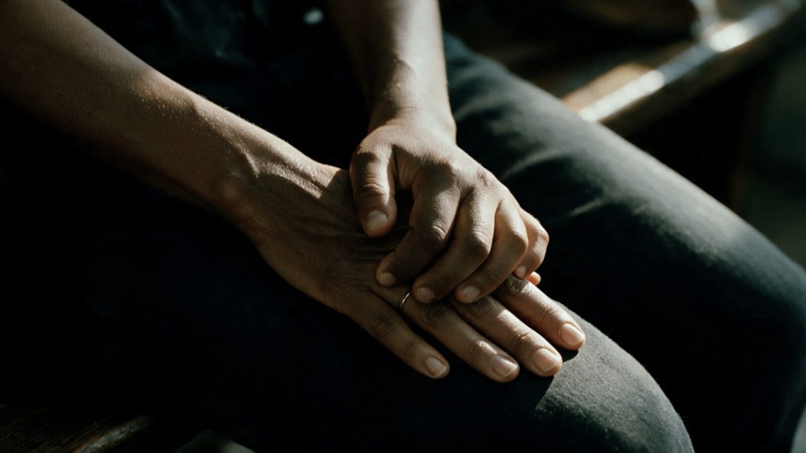 Close-up of clasped hands resting on a knee.
