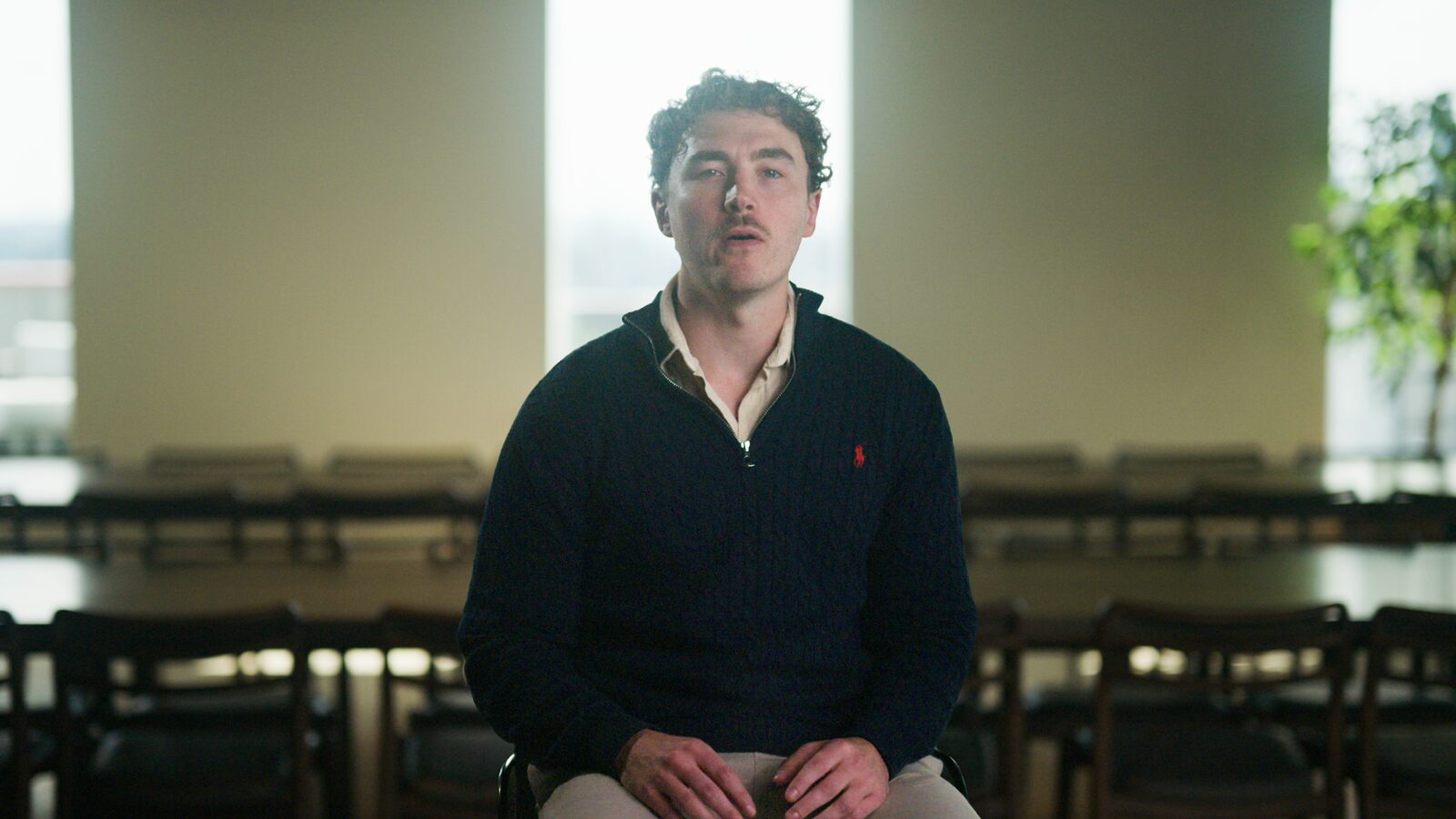 A founder in a navy jumper, seated in an empty meeting room.